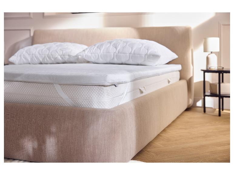 Chambre avec un lit comprenant un surmatelas, un matelas et deux oreillers.