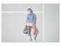 Une femme portant un polo bleu et une jupe blanche tient une raquette de paddle.