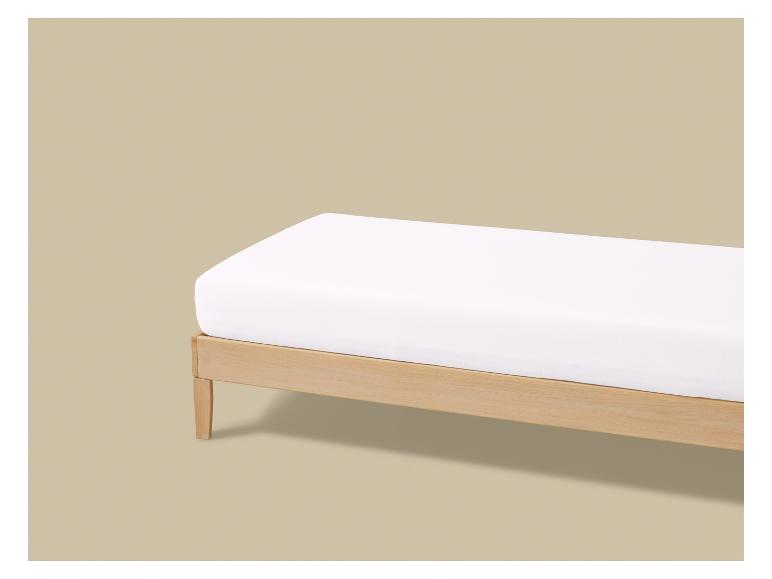 Lit en bois avec matelas blanc sur fond beige.