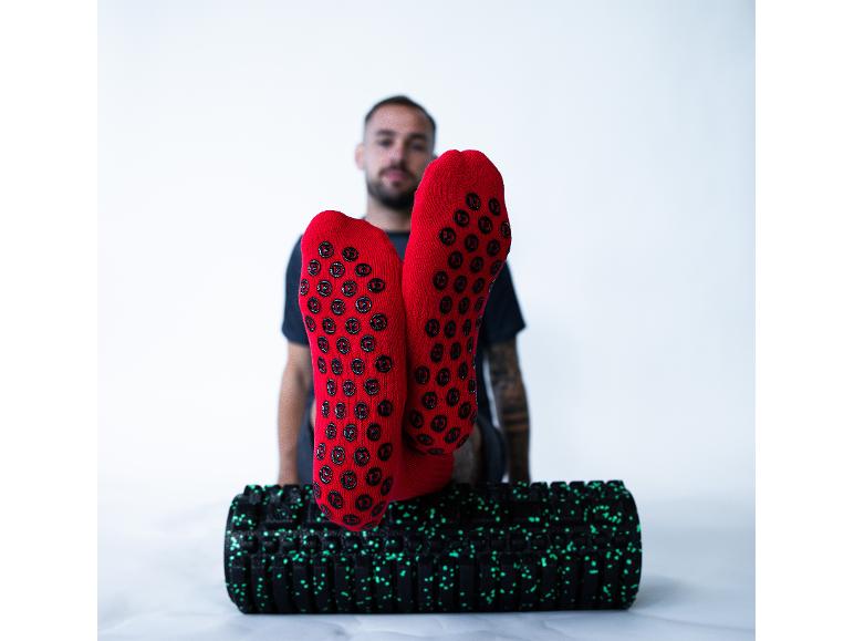 Homme en chaussettes antidérapantes rouges, pieds sur rouleau de massage noir.