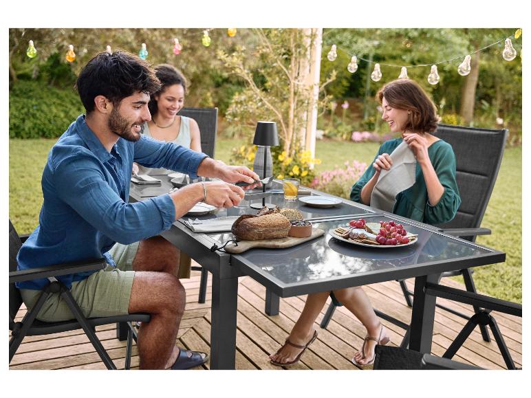 Trois personnes profitent d'un repas en plein air sur une terrasse avec table et chaises de jardin.