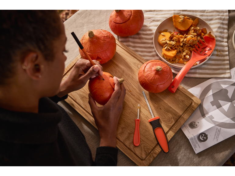 Personne sculptant des citrouilles d'Halloween avec des outils de sculpture et des graines.