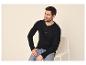Homme en chemise Henley noire à manches longues et jean, assis sur une chaise.