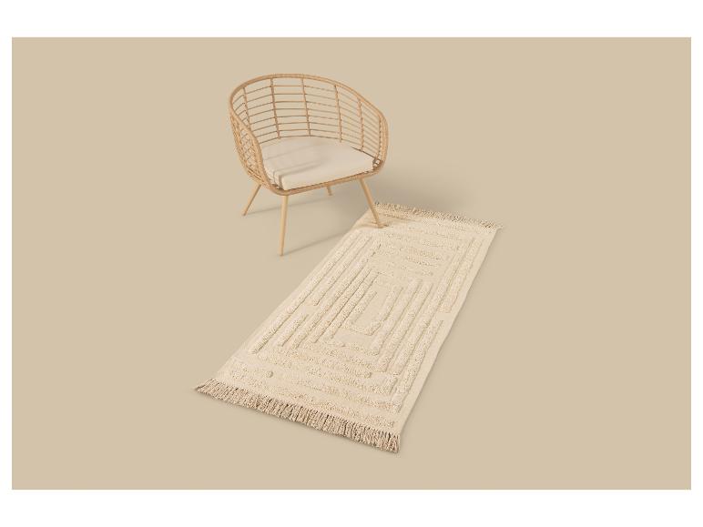 Fauteuil en osier avec coussin crème et tapis rectangulaire à motif géométrique.