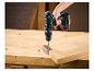 Perceuse sans fil verte et noire fixant une charnière métallique sur une planche en bois.
