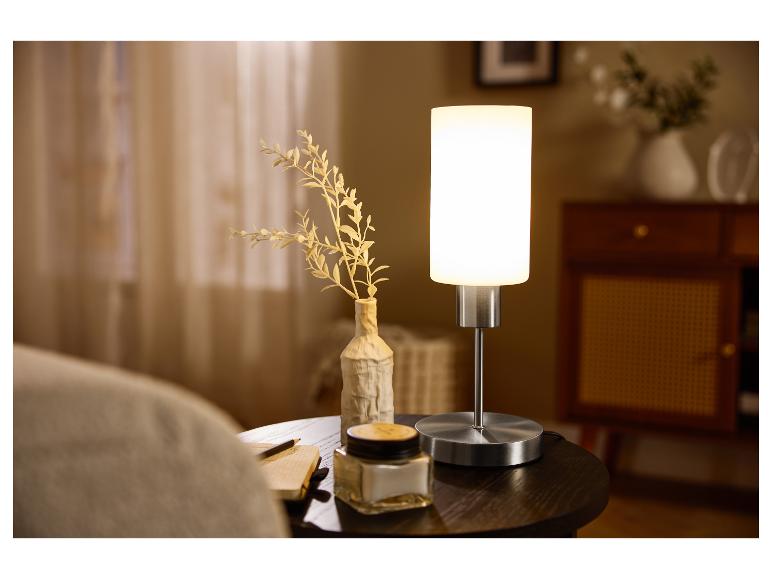 Lampe de table avec abat-jour blanc et base métallique sur une table de chevet décorée.