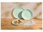 Assiettes vert menthe avec crêpes et baies, et couverts sur une table en bois.