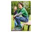 Homme en t-shirt vert et salopette en jean, portant des baskets vertes, assis sur un banc en bois.