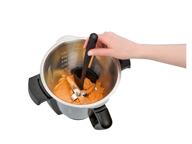 Une main utilisant une spatule dans un robot culinaire avec de la purée d'orange.