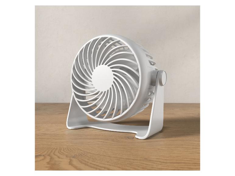Petit ventilateur blanc sur une table en bois.