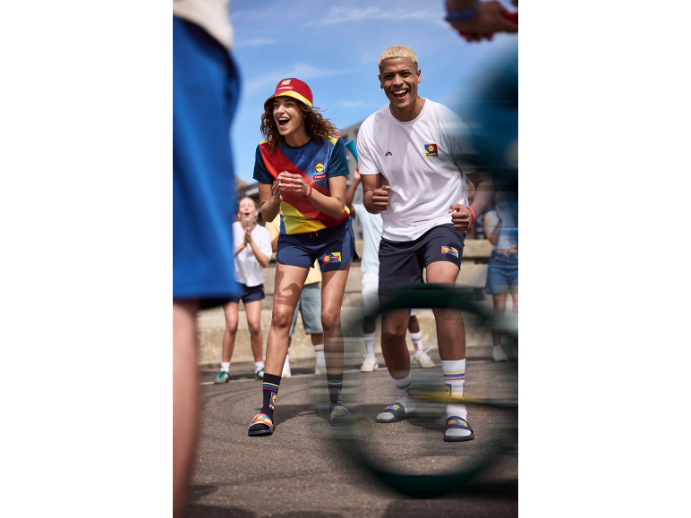 Deux personnes en tenue de sport colorée, bob, t-shirts, shorts, chaussettes et claquettes, acclamant.