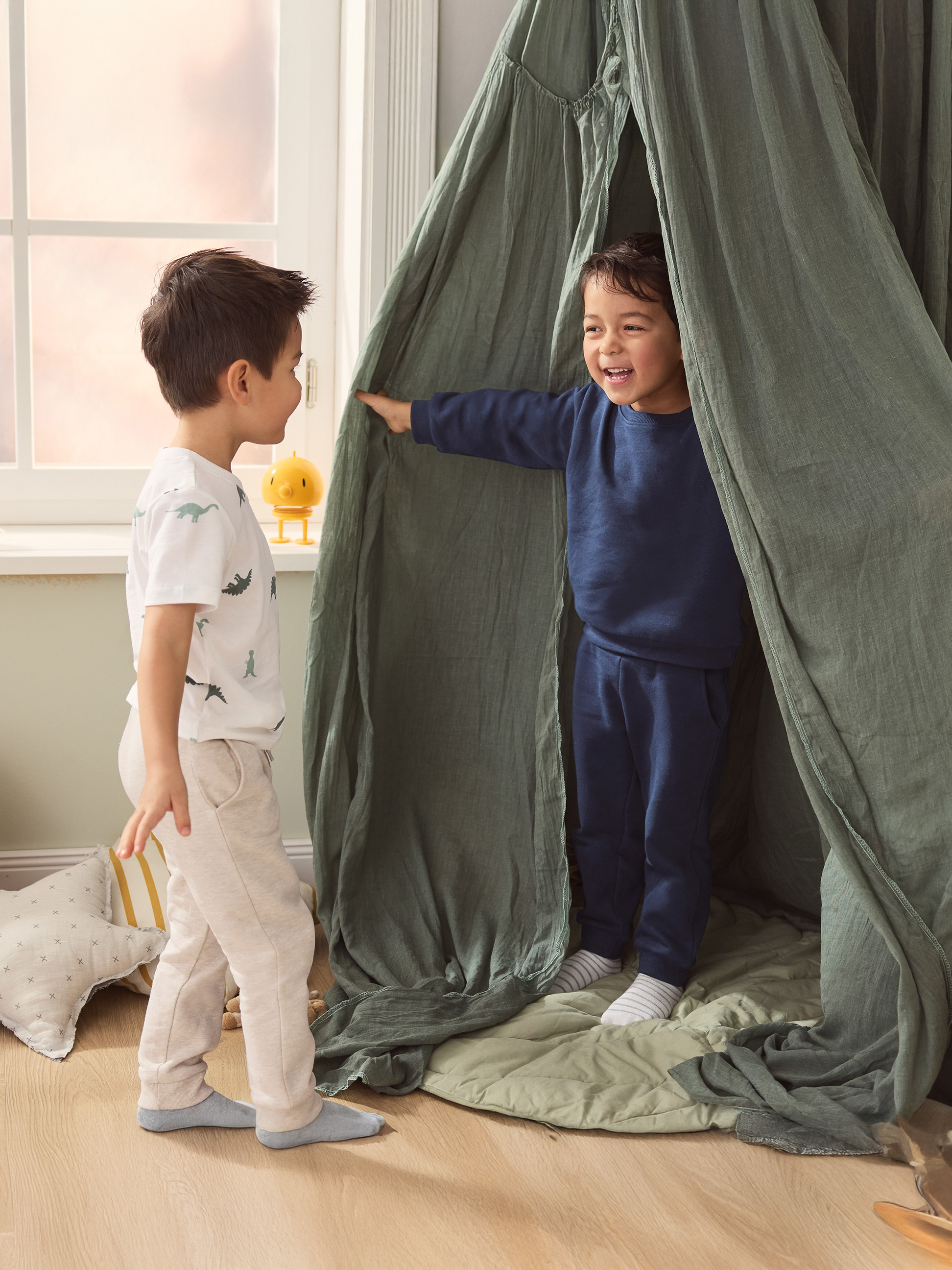Deux garçons jouent dans une tente de jeu verte, l'un portant un t-shirt à dinosaures.