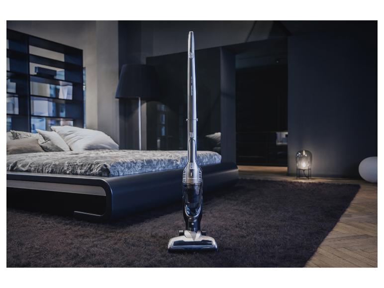 Un aspirateur balai Grundig dans une chambre moderne avec un lit et un tapis.