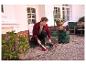 Homme balayant des feuilles avec un balai et une pelle dans un sac vert pour déchets de jardin.