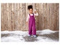 Une fille portant une salopette violette et des bottes bleues joue dans la neige.