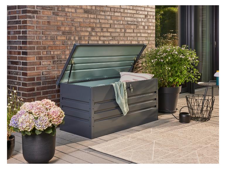Coffre de rangement de jardin gris foncé avec couvercle ouvert, à côté de plantes en pot sur une terrasse.