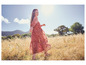Une femme marche dans un champ avec une longue robe rouge à imprimé floral.