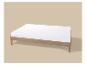Lit en bois avec matelas blanc sur fond beige.