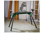 Une table de scie verte avec des pieds et une scie mobile.