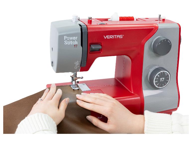 Machine à coudre rouge et grise en utilisation, mains guidant le tissu marron.