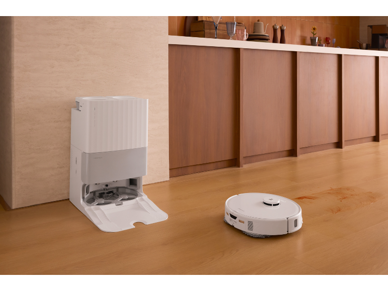 Aspirateur robot blanc avec sa station de charge sur un parquet de cuisine.