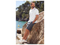 Un homme en polo blanc et short gris au bord de la mer.