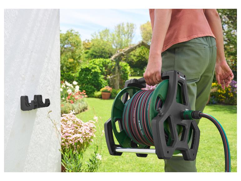 Personne tenant un tuyau d'arrosage Parkside sur un support dans un jardin.