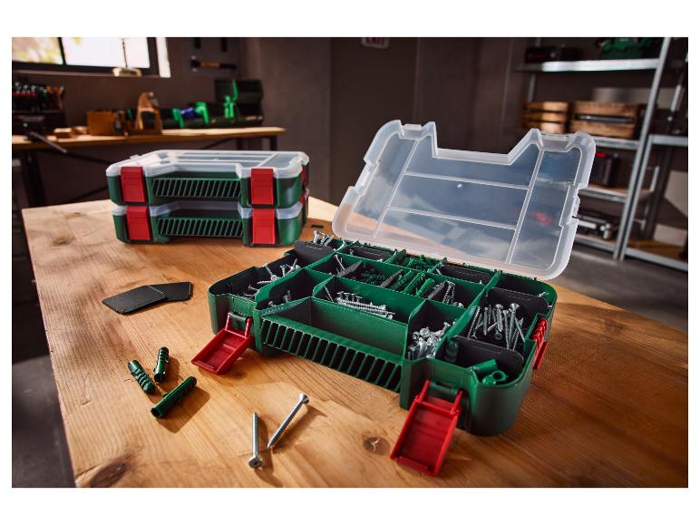 Boîte à outils ouverte avec vis et chevilles sur une table en bois, deux boîtes fermées en arrière-plan.