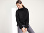 Une femme porte un pull noir à col roulé et un jean gris.