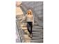 Femme en cardigan beige et leggings en similicuir noir sur des escaliers en béton.