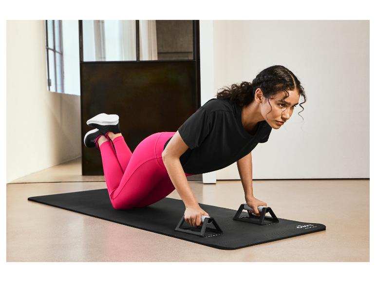 Une femme faisant des pompes sur un tapis de yoga noir avec des poignées pour pompes.