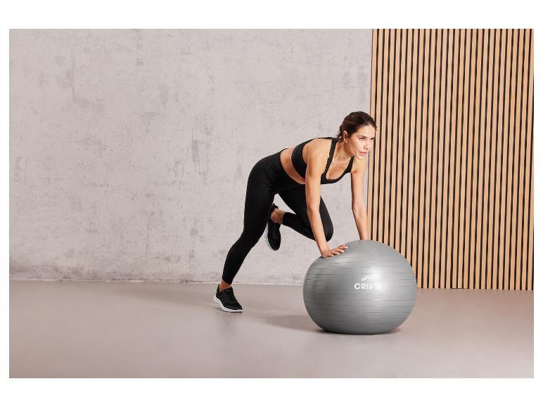 Une femme fait des exercices avec un ballon de fitness gris de Crivit.