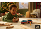Enfant jouant avec un train en bois près d'un sapin de Noël.
