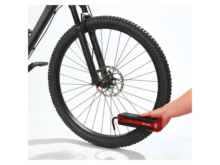 La main d'une personne tient un compresseur d'air portable rouge et noir pour gonfler un pneu de vélo.