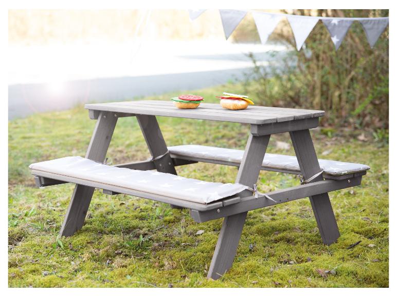 Table de pique-nique grise pour enfants avec coussins et nourriture jouet sur l'herbe.