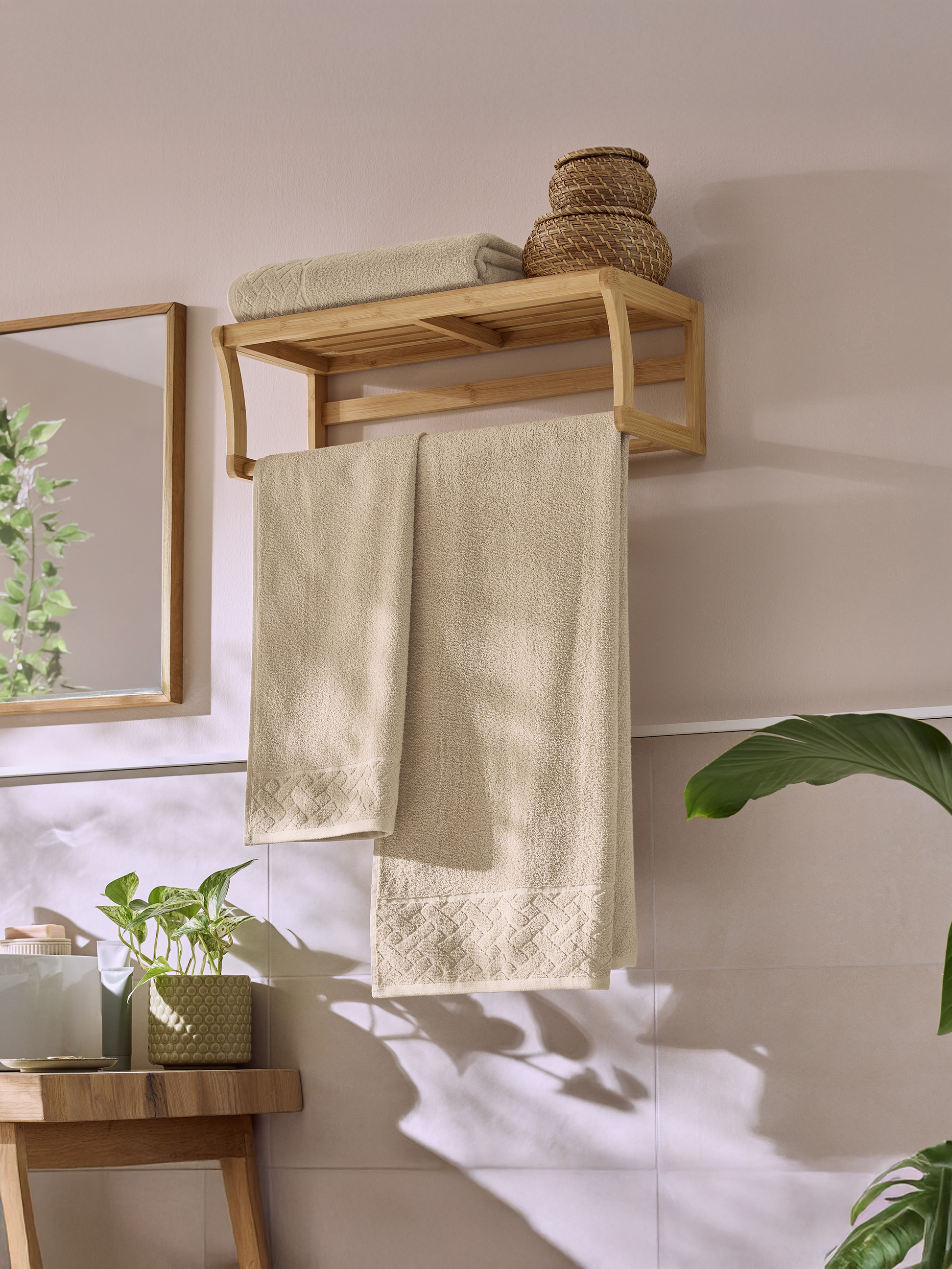 Salle de bain avec un porte-serviettes en bois, des serviettes beiges et des plantes vertes.