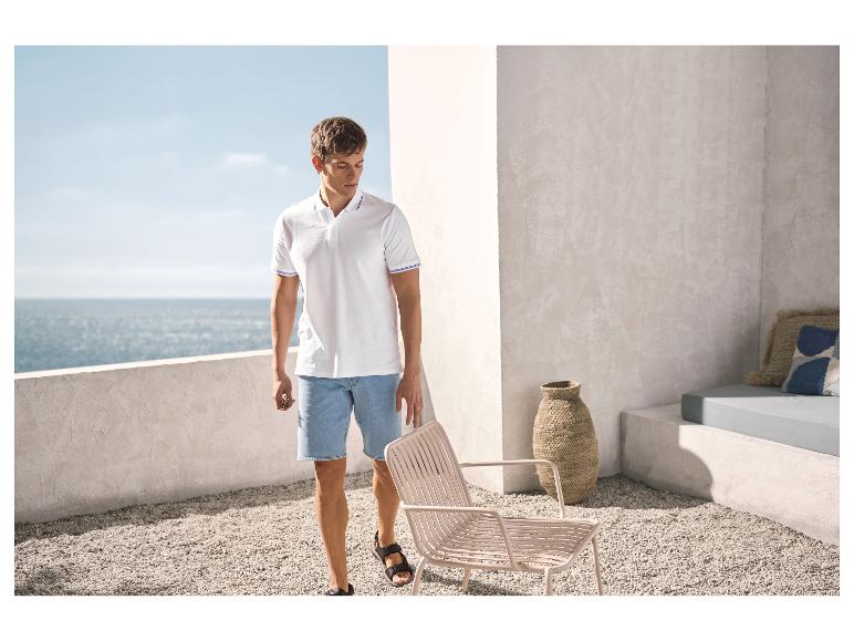 Homme en polo blanc et short en jean sur une terrasse avec vue sur la mer.