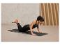 Une femme fait des pompes sur un tapis de yoga noir.