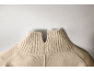 Gros plan sur un pull en maille beige avec un col montant côtelé et une petite fente en V.