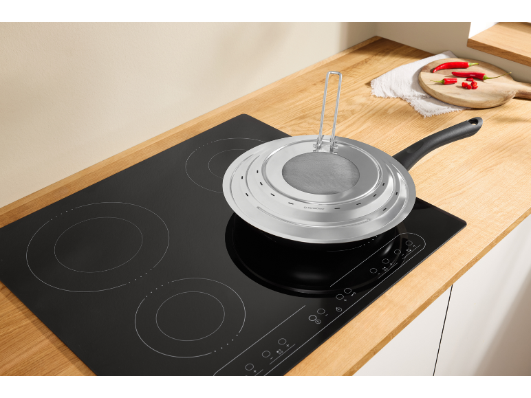 Poêle à frire avec couvercle anti-éclaboussures sur une plaque à induction dans une cuisine.