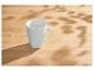 Tasse blanche sur une table en bois avec des ombres de feuilles.