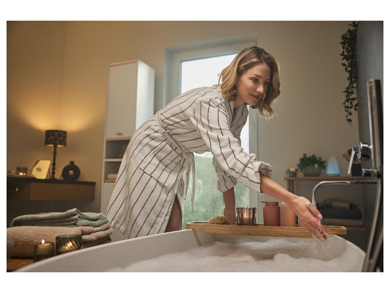 Une femme en peignoir prépare un bain moussant.