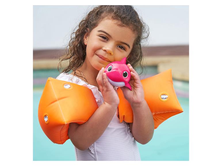 Fille souriante avec des brassards de natation orange et un jouet Baby Shark rose