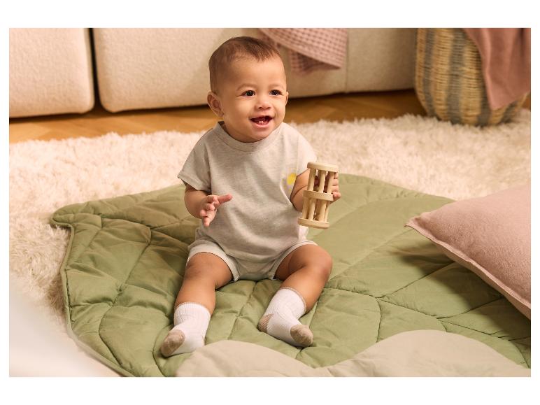Bébé souriant assis sur un tapis vert, tenant un hochet en bois.