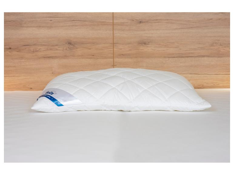 Oreiller blanc matelassé sur un lit avec une tête de lit en bois.