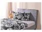Un lit avec une tête de lit grise et un ensemble de draps tropicaux noir et blanc.