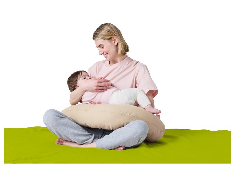 Mère souriante allaitant son bébé sur un coussin d'allaitement, assise sur un tapis vert.