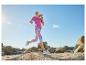 Femme courant en t-shirt fuchsia et leggings à motifs dans un paysage rocheux sous un ciel bleu.