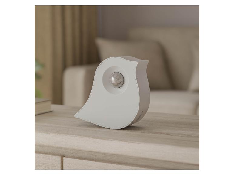 Capteur de mouvement blanc en forme d'oiseau sur une table en bois dans un salon.