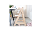 Chaise haute en bois clair avec plateau, à côté d'une table avec vaisselle pour enfants.